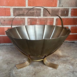 May include: A vintage metal basket with a scalloped rim and a handle. The basket is supported by a gold-toned metal stand with curved legs. The basket is made of a silver-colored metal.