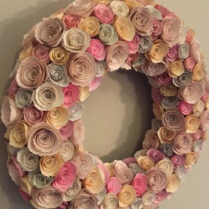 May include: A paper flower wreath with pink, beige, and yellow flowers. The wreath is made of many individual paper flowers, each with a pearl in the center.