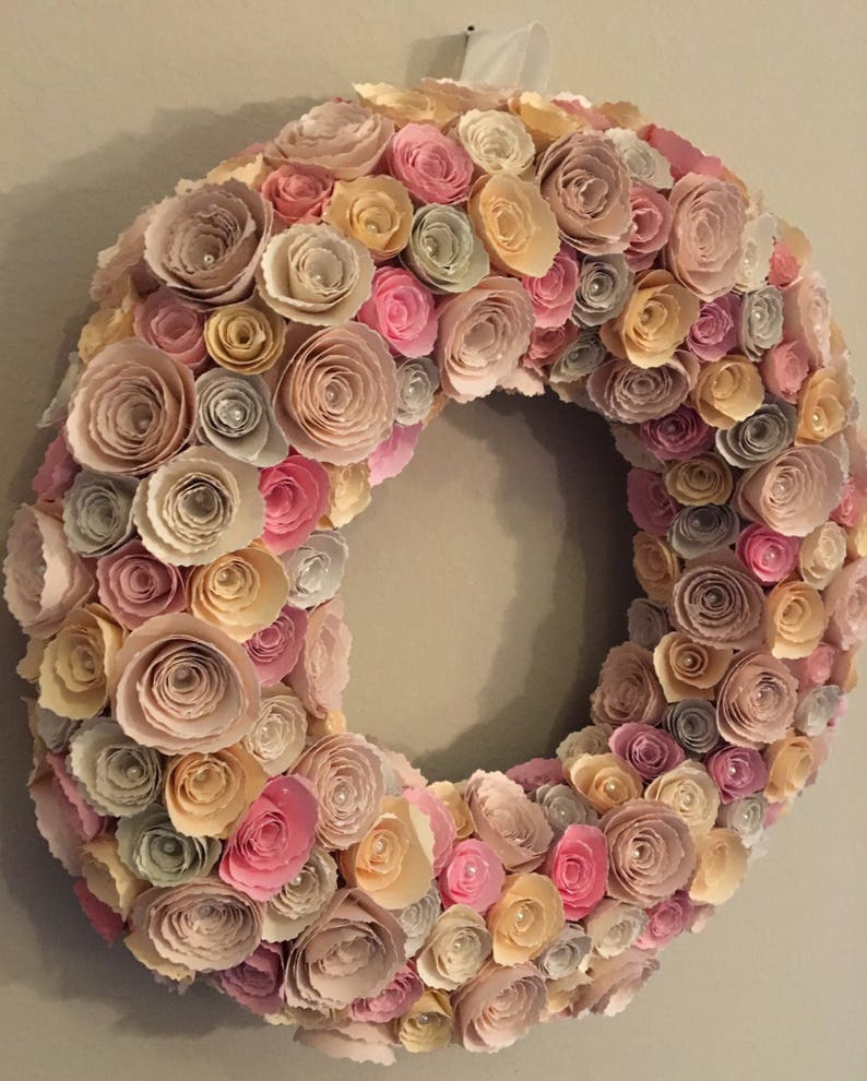 May include: A paper flower wreath with pink, beige, and yellow flowers. The wreath is made of many individual paper flowers, each with a pearl in the center.