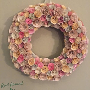 May include: A wreath made of paper roses in shades of pink, beige, and cream. The wreath is decorated with small pearl-like embellishments. The text "Reid Around the Rosies Paper Creations" is at the bottom of the image.