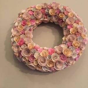 May include: A paper flower wreath with pink, cream, and beige paper flowers. The wreath is made of many small paper flowers that are arranged in a circle.