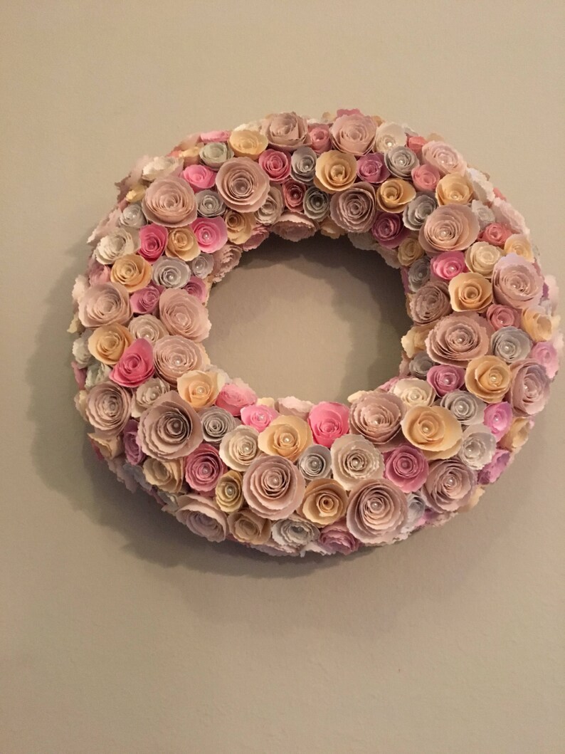 May include: A paper flower wreath with pink, cream, and beige paper flowers. The wreath is made of many small paper flowers that are arranged in a circle.