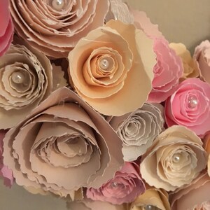 May include: A close-up of a paper flower wreath with pink, peach, and cream colored flowers. Each flower has a pearl in the center.