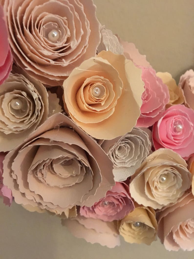 May include: A close-up of a paper flower wreath with pink, peach, and cream colored flowers. Each flower has a pearl in the center.