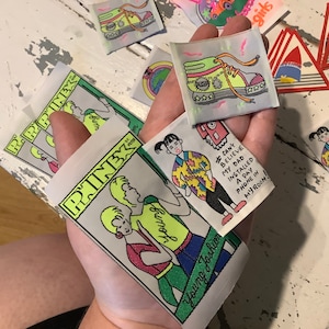 Peut inclure: Un ensemble de patchs thermocollants illustrant des dessins colorés. Un patch représente deux personnes avec le texte "Young Fashion" et "PINK". Un autre patch représente une personne avec le texte "Je n'arrive pas à croire que mon père a installé un téléphone payant dans ma chambre !". Un autre patch représente une paire de rollers avec le texte "ST. PETER" dessus.