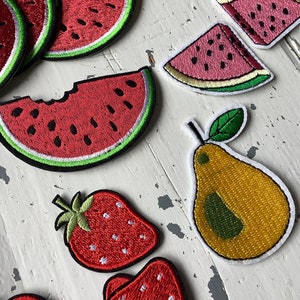 Op de afbeelding: Een set geborduurde strijk-op patches met verschillende vruchten, waaronder watermeloen, peer en aardbeien. De patches zijn kleurrijk en gedetailleerd, perfect om een vleugje whimsy toe te voegen aan kleding, tassen of andere accessoires.