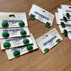 May include: Assortment of green and gold fabric covered buttons with the text "Dressmakers Supply" and a phone number on the packaging.