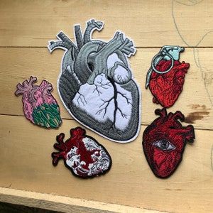 May include: Five embroidered patches featuring anatomical hearts. One heart is gray and white, one is pink and green, one is red with a white eye, one is red with a white outline, and one is red with a white outline and a blue and white grenade.