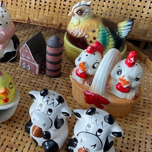 Könnte beinhalten: Eine Sammlung von Salz- und Pfefferstreuern aus Keramik mit verschiedenen Designs, darunter ein Bauernhaus, ein Hahn, eine Kuh und ein Huhn. Die Streuer sind in leuchtenden Farben bemalt und haben einen verspielten Stil.