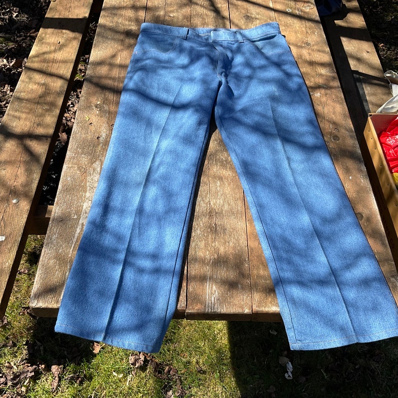 Op de afbeelding: Een paar blauwe spijkerbroeken met een rechte pijp. De broek ligt plat op een houten oppervlak.