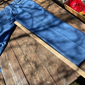 Op de afbeelding: Een paar blauwe denim jeans plat gelegd op een houten oppervlak met een meetlint ernaast. De jeans is lichtblauw en heeft een rechte pijp.