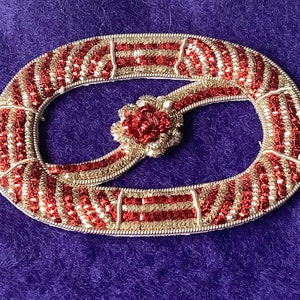 Peut inclure: Un motif ovale en perles rouges et dorées avec une petite fleur en perles rouges au centre.
