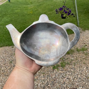 May include: A silver metal teapot-shaped serving dish. The dish is made of metal and has a shiny, reflective surface.