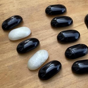 Può includere: Un set di pietre ovali di colore nero e bianco. Le pietre sono lisce e lucide. Ci sono otto pietre nere e due pietre bianche.