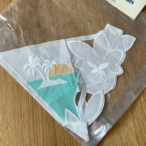 Könnte beinhalten: Weiße Baumwoll-Applikation mit floralem Design und einer türkisblauen gestickten Szene mit einer Palme und einer untergehenden Sonne.