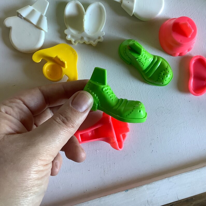Może przedstawiać: Zestaw kolorowych plastikowych zabawek w kształcie buta, rękawiczki, kapelusza, kwiatu i buta. Elementy są przeznaczone do zabawy dla dzieci i wykonane są z trwałego plastiku.