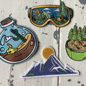 May include: Five embroidered iron-on patches featuring a mountain range, a bottle with a cactus inside, a pair of goggles, a cup of coffee with trees, and a yellow sun.