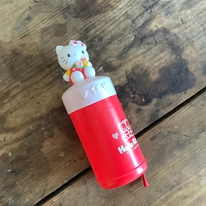 May include: Red plastic Hello Kitty water bottle with a white lid and a Hello Kitty character on top. The bottle has a white heart and the text "Hello Kitty" on the side.