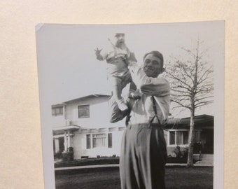 Old photo of father lifting baby in the air, son or daughter looking a little alarmed, happy dad kid candid family black white photograph