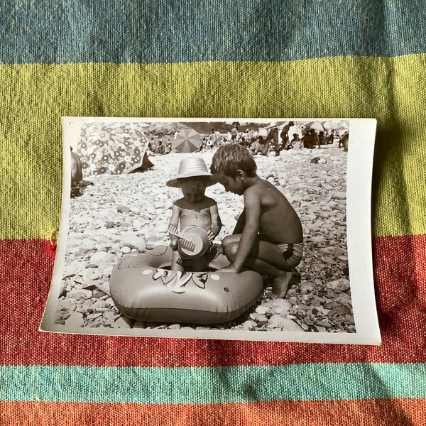 Single vintage photograph of two kids on the beach with toy, candid snapshot black and white family photo from album 1950s 60s 70s boys play