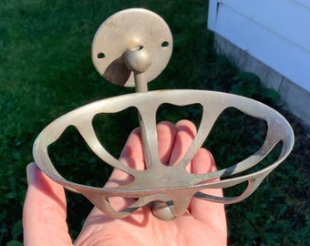 Puede incluir: Un jabonera vintage plateada con un diseño calado decorativo. La jabonera está unida a un soporte de pared con una placa redonda en la parte posterior.