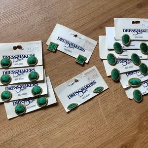 May include: Assortment of green and gold fabric covered buttons with the text "Dressmakers Supply" and a phone number. The buttons are packaged on white cards.