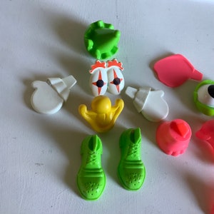 Może przedstawiać: Zestaw kolorowych plastikowych zabawek do zabawki z głową ziemniaka. Zestaw zawiera zielony kapelusz, dwa zielone buty, dwie białe rękawiczki, ż&oacute;łty nos, dwa czerwone oczy z czarnymi źrenicami, r&oacute;żowe usta i r&oacute;żowe ucho.