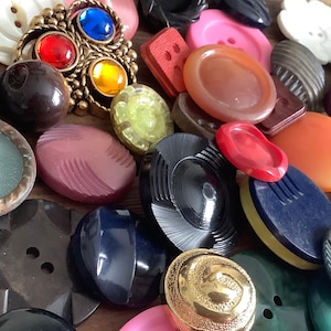 May include: A collection of vintage buttons in various colours, shapes, and sizes. The buttons are made from different materials, including plastic, metal, and wood. Some of the buttons have intricate designs, while others are simple and plain.