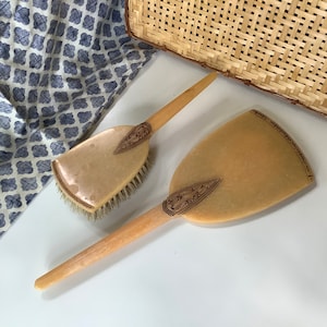 May include: A set of two vintage ivory-colored hair brushes with intricate brown floral designs. The brushes have wooden handles and are in excellent condition.
