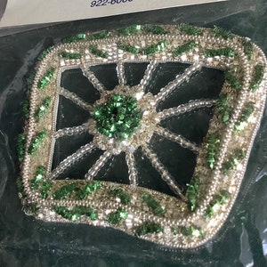 May include: A green and silver beaded embellishment with a square frame and a starburst design in the center.