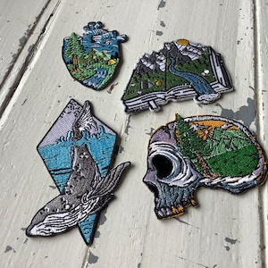 Peut inclure: Ensemble de quatre patchs brodés thermocollants représentant une baleine, un crâne avec une scène de montagne à l'intérieur, un cœur avec une scène de montagne à l'intérieur et un livre avec une scène de montagne à l'intérieur.