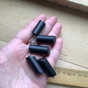 May include: Five black wooden curtain tiebacks with silver metal hooks. The tiebacks are cylindrical in shape and are arranged in a pile.