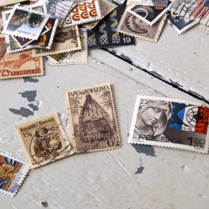 May include: A collection of vintage postage stamps from various countries, including Canada, Denmark, Papua New Guinea, Poland, and the Philippines. The stamps feature a variety of designs, including a hut, a woman's face, and a ship.