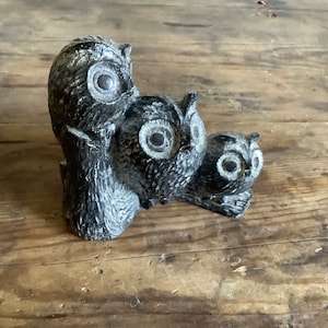 May include: A carved stone sculpture of three owls, with the top owl perched on the back of the middle owl, and the bottom owl sitting on a wooden surface.