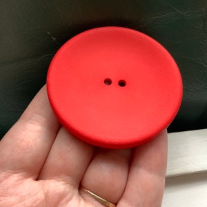 Peut inclure: Un grand bouton rond de couleur rouge vif avec deux trous au centre.