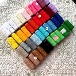 May include: A collection of colourful spools of thread, some with numbers on them, arranged in a triangular pattern on a white quilted fabric.