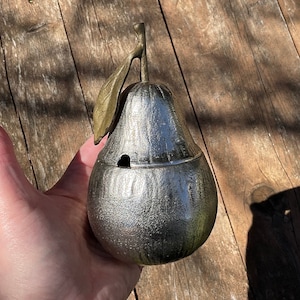 Könnte beinhalten: Ein silbernes, birnenförmiges Dekorationsobjekt mit einem goldenen Blattdesign. Die Birne ist aus Metall und hat eine strukturierte Oberfläche.