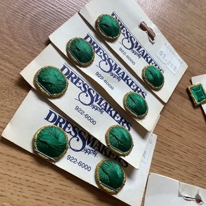 May include: Six green and gold fabric covered buttons on white cards with the text "Dressmakers Supply" and the phone number 922-6000. The price is $1.99.