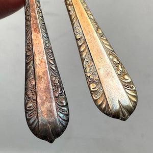 May include: Two silver-plated forks with ornate floral designs on the handles. The forks have a vintage look and are slightly tarnished.