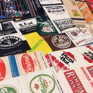 May include: A collection of vintage matchbook covers featuring various businesses and brands, including The Old Firehall, The Keg, Pizza Hut, Ramada Inns, and Ukrainian Caravan. The matchbooks are in various colors and designs, with some featuring logos, text, and illustrations.