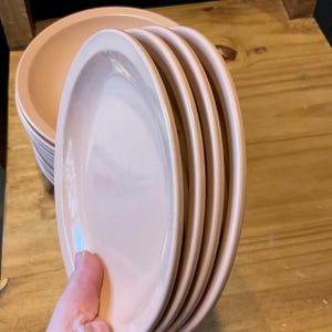 K&ouml;nnte beinhalten: Ein Stapel von sechs rosafarbenen Keramik-Dinnertellern. Die Teller sind &uuml;bereinander gestapelt, wobei der oberste Teller der gr&ouml;&szlig;te ist.