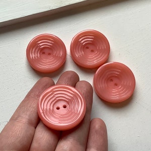 May include: Four pink plastic buttons with a swirl design. The buttons have two holes each.