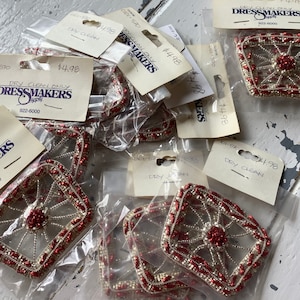 May include: A close-up of several red and silver beaded embellishments, each in a clear plastic bag with a price tag. The tags read "Dressmakers" and "Dry Clean Only".