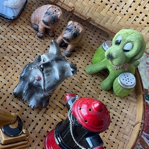 May include: A set of six salt and pepper shakers featuring various animal designs. The shakers are made of ceramic and are painted in a variety of colors. The set includes a black and white terrier, a brown and white pug, a green frog, a brown and white dog, a brown and white dog, and a red fire hydrant.