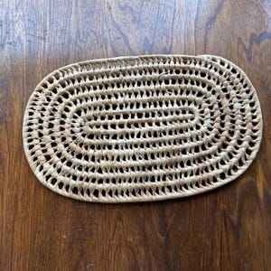 May include: Oval woven wicker coaster in a natural brown colour.