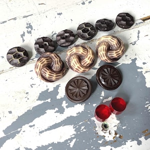 May include: Assortment of brown and white plastic buttons with intricate designs. Some buttons have a swirl pattern, while others have a geometric design. There are also two red glass buttons.