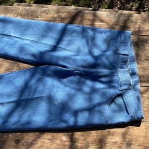 Op de afbeelding: Een paar blauwe denim jeans gevouwen in de helft, met de voor- en achterzakken zichtbaar. De jeans is lichtblauw gewassen en heeft een klassieke rechte pijp.