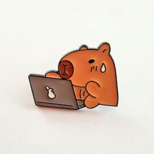 Op de afbeelding: Een oranje cartoon capibara met zwarte contouren die op een grijze laptop werkt. De capibara heeft een bezorgde uitdrukking. De laptop heeft een wit Apple-logo. Een pin.