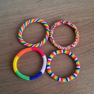 Peut inclure: Quatre bracelets en perles colorées avec un motif arc-en-ciel. Les bracelets sont faits de petites perles colorées et sont disposés en cercle.