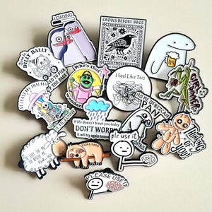 Peut inclure: Une collection d'épingles émaillées colorées avec divers motifs et textes. Les épingles présentent des personnages de dessins animés, des animaux et des phrases comme "Crows Before Bros", "Girl Dinner" et "Please Use It".